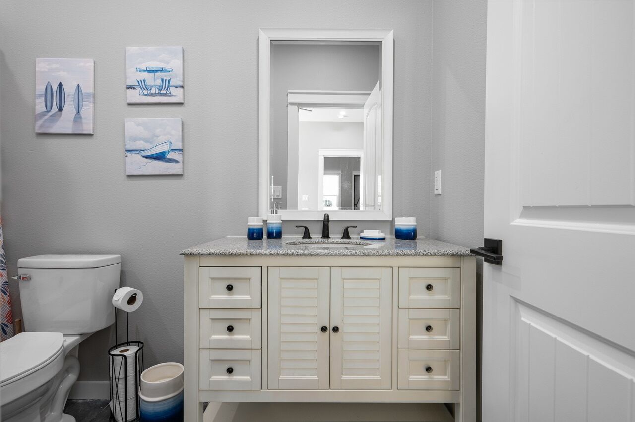 A bathroom with a toilet, sink, and cabinet. There are three framed pictures on the wall.