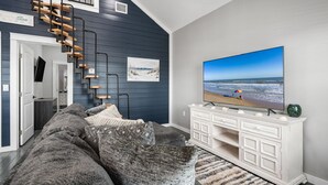 Een moderne woonkamer met een grote flatscreen-tv, een donkerblauwe accentmuur, een witte console en een trap met houten treden.