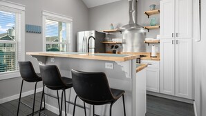 Een moderne keuken met een centraal eiland, barstoelen, witte kasten en een groot raam.