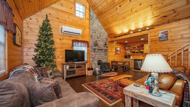 A cozy log cabin interior with a fireplace, a television, a stone wall, and a dining area. - Charming Dog Friendly Retreat w/ Hot Tub (McHenry)