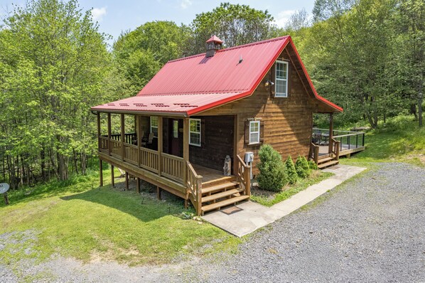 A wooden cabin with a red roof, a porch, and a small deck.