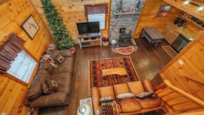A cozy cabin interior with a wooden interior, a fireplace, a television, and a Christmas tree. - Charming Dog Friendly Retreat w/ Hot Tub (McHenry)