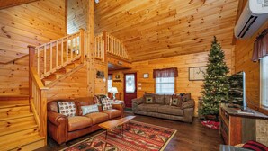 A cozy log cabin interior with a wooden staircase, two leather sofas, a Christmas tree, and a fireplace. - Charming Dog Friendly Retreat w/ Hot Tub (McHenry)