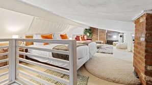 Una camera da letto con un letto, cuscini, un baldacchino bianco, un muro in mattoni e un tavolino con una pianta.
