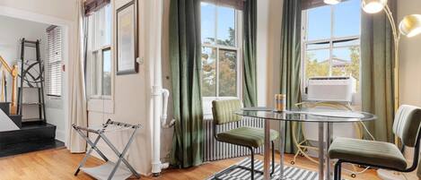 A room with a glass table, two chairs, a radiator, and a window with curtains.
