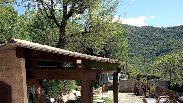 A rustic outdoor patio with a wooden pergola, a barbecue area, and a seating arrangement.