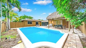 Un jardin avec une piscine, une clôture en bois et une structure recouverte d’un toit de chaume.