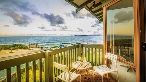 A balcony with two white chairs and a table, overlooking a coastal view with the ocean and a clear sky. - Absolute Beachfront Port Elliot | Ocean Views | Sleeps 8 | Family Holiday Accommodation (Port Elliot)