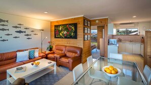 A modern living room with a brown leather sofa, a glass dining table, and a kitchen in the background. - Absolute Beachfront Port Elliot | Ocean Views | Sleeps 8 | Family Holiday Accommodation (Port Elliot)