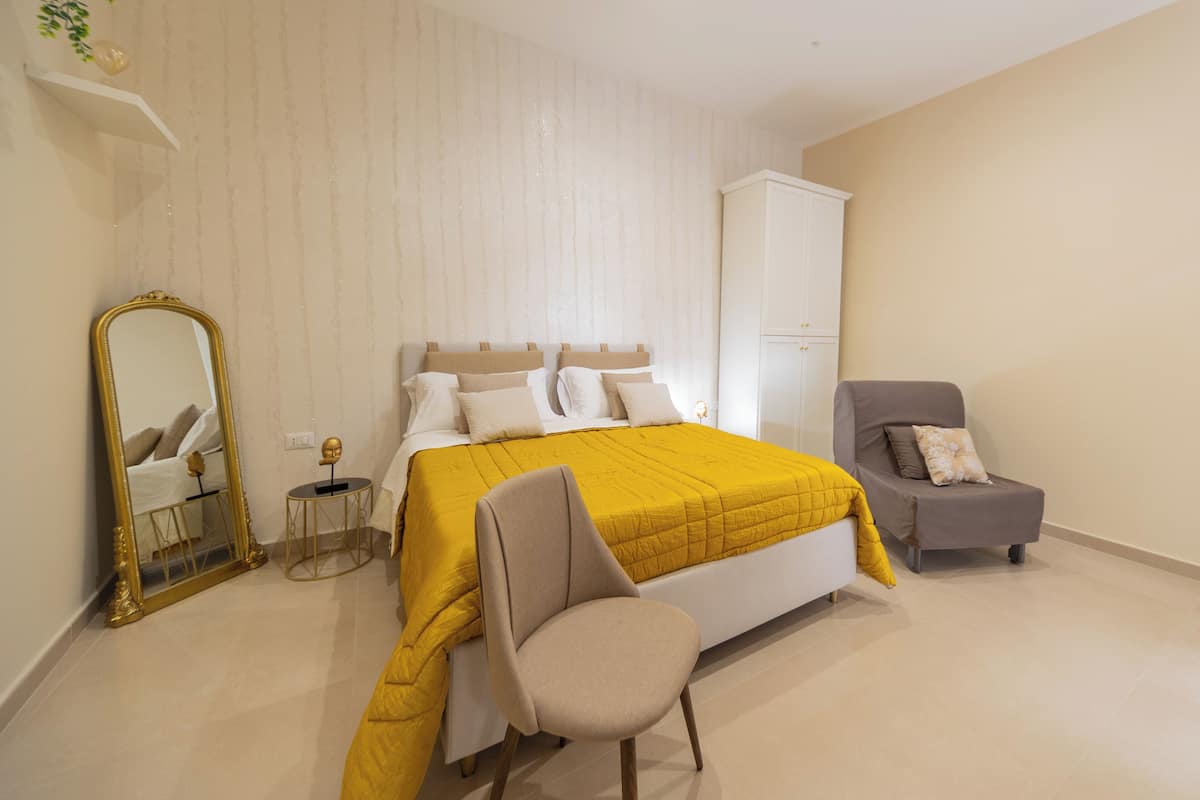 A bedroom with a bed, a chair, a cabinet, and a mirror.