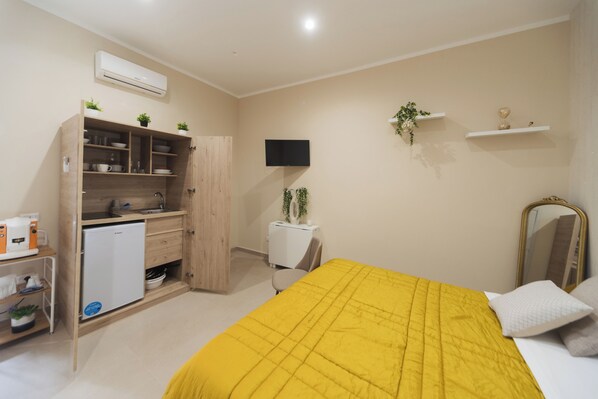 Un dormitorio con cama, armario, refrigerador pequeño, televisor y espejo.