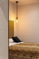 Un dormitorio con una cama que presenta una colcha de estampado de leopardo, un almohilar negro y un cabecero con rayas horizontales.