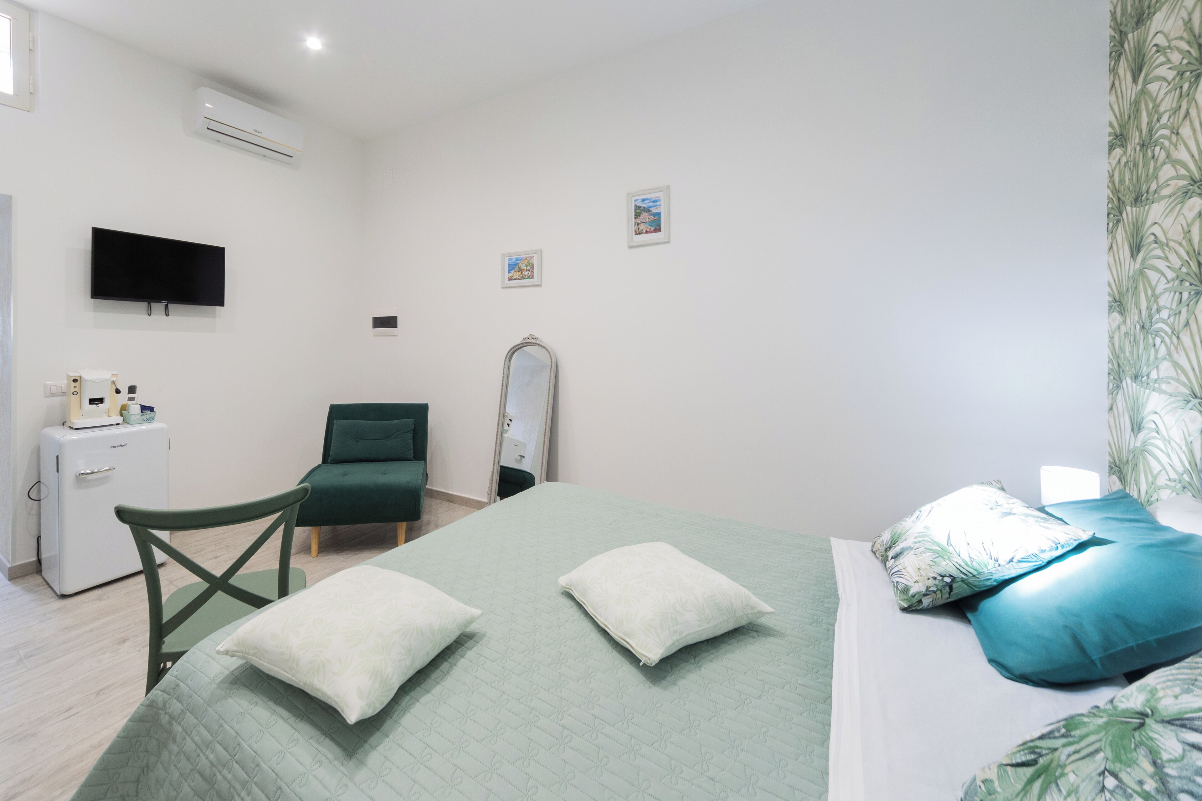 A bedroom with a bed, a chair, a desk, a TV, and a small fridge.