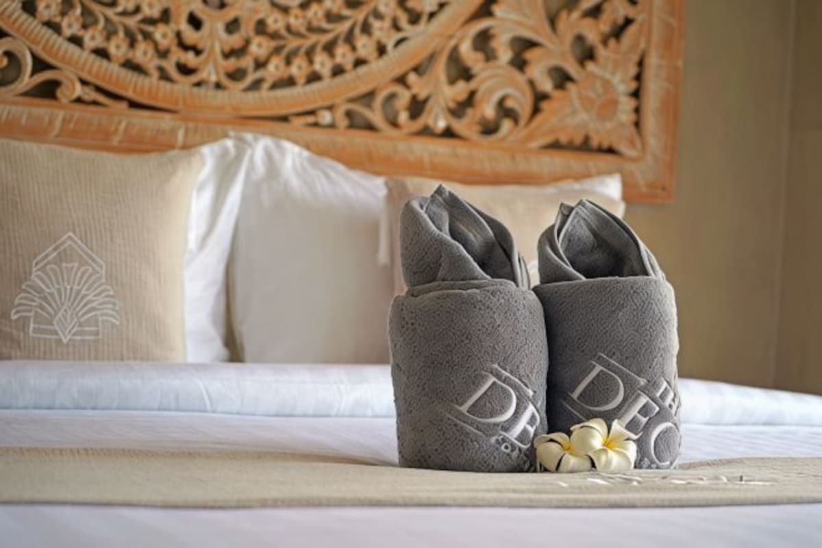 A neatly made bed with a decorative headboard, a pair of folded towels, and a small decorative item on the bed.
