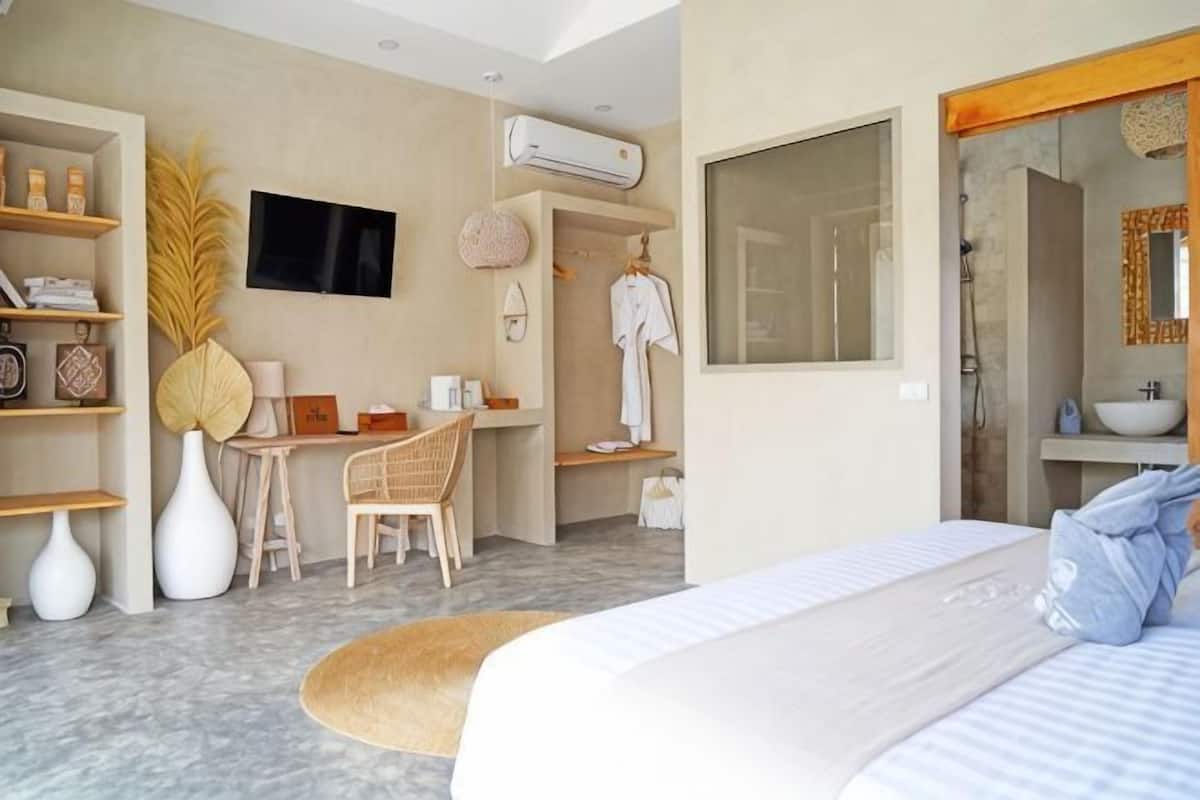 A modern hotel room with a bed, a desk, a chair, a TV, and a bathroom visible through an open door.