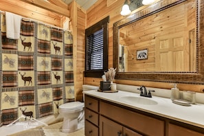 Bagno con arredamento in legno, un water bianco, un lavandino con specchio e una tenda da doccia con stampe animalier.