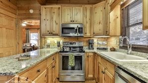 A kitchen with wooden cabinets, granite countertops, stainless steel appliances, and a window with blinds. - Sweet Water Retreat | No Pet Fees | Sleeps 5 | Coosawattee Riverfront (Ellijay)