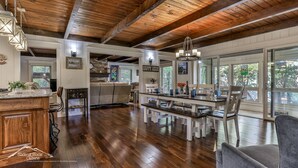 A spacious kitchen with wooden flooring, a dining area with benches, and large windows offering a view of the outdoors. - Lake Reflections | Sleeps 6 | No Pet Fee | lakefront w/dock | paved | Hot Tub (Hiawassee)
