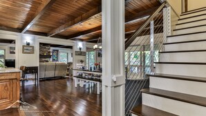 A spacious living area with a wooden ceiling, a dining area with a bar, and a staircase with a metal railing. - Lake Reflections | Sleeps 6 | No Pet Fee | lakefront w/dock | paved | Hot Tub (Hiawassee)