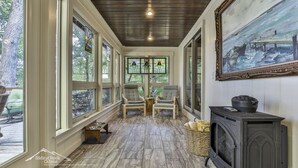 A cozy cabin interior with large windows, a fireplace, and a painting on the wall. - Lake Reflections | Sleeps 6 | No Pet Fee | lakefront w/dock | paved | Hot Tub (Hiawassee)