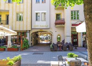 An outdoor cafe area with tables and chairs, a building with a sign reading "TRZY CRACUE", and a tree in the foreground. - Imperial Apartments - Monte Deluxe (Sopot)