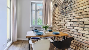 Un comedor con pared de ladrillo, una ventana con cortinas y una mesa dispuesta con platos azules y sillas blancas.