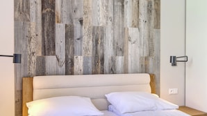 Una cama con sábanas blancas, cabecera de madera y una pared con diseño rústico de paneles de madera.