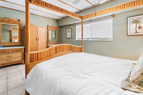 A four-poster bed with a white bedspread, wooden headboard, and footboard, flanked by a wooden wardrobe and a mirror.