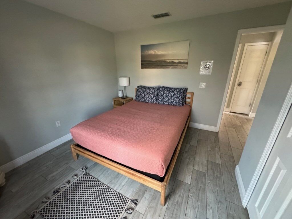 A bedroom with a bed, a nightstand, a lamp, a rug, and a door.