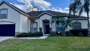 A two-story house with a garage, a covered entryway, and a front yard with palm trees. - Hampton Lakes Villa 5 Bedroom Home (Davenport)