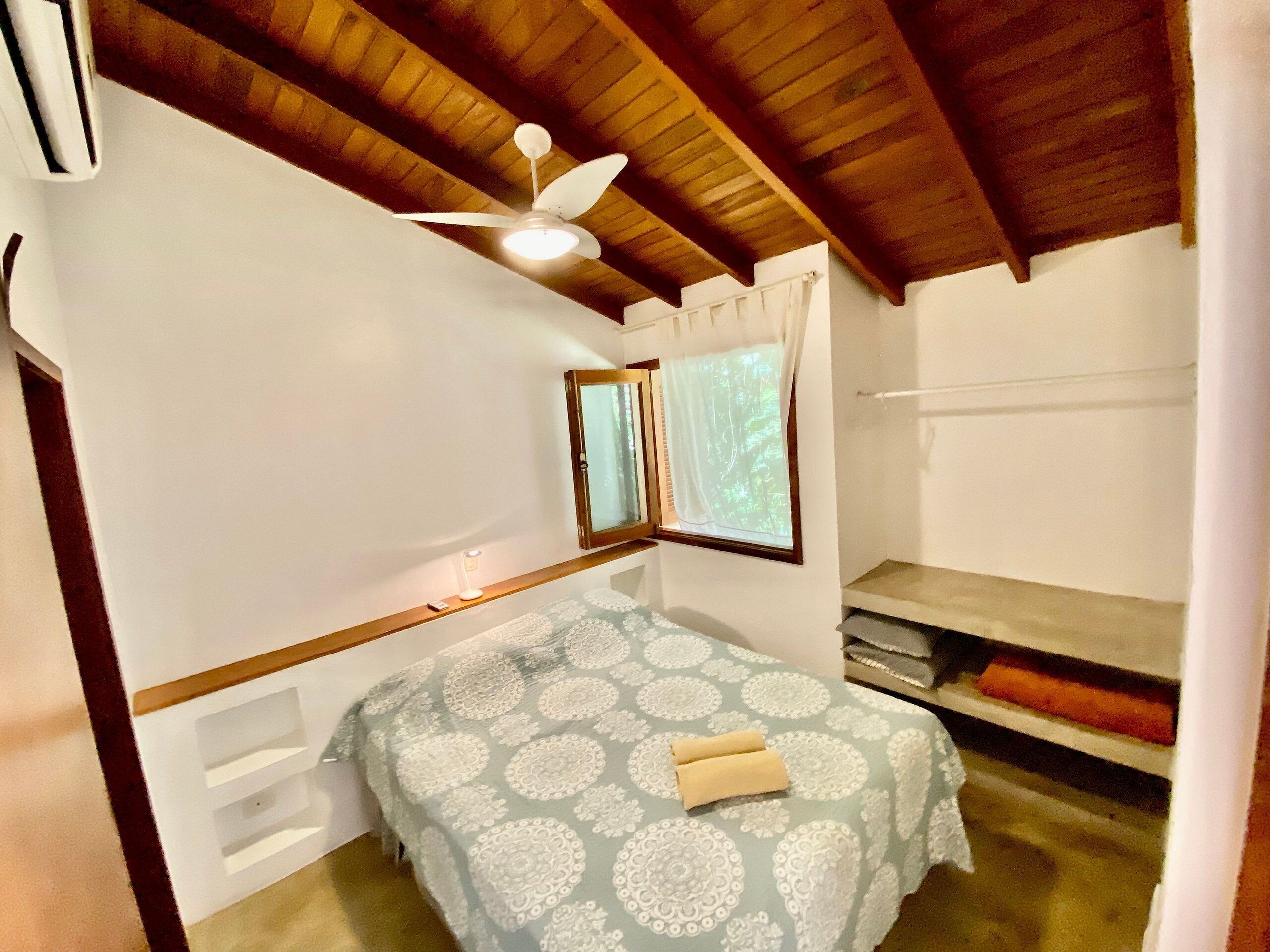 A small, cozy room with a single bed, a ceiling fan, a window with curtains, and a small shelf.