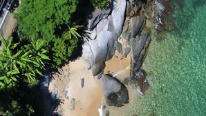 An aerial view of a beach with clear turquoise water, sandy shore, and large rocks.