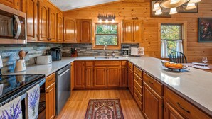 A kitchen with wooden cabinets, a stainless steel microwave, a sink, and a window with a view of trees.