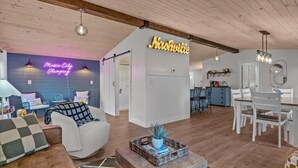 Tilava olohuone, jossa on neonvalomainos, jossa lukee ”Nashville”, valkoisilla huonekaluilla sisustettu ruokailutila ja taustalla keittiö.