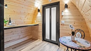 Puinen sisustus, jossa on mustakehyksinen ovi, pieni pöytä mosaiikkikuvioisella pöytäliinalla ja ruukussa oleva kasvi.