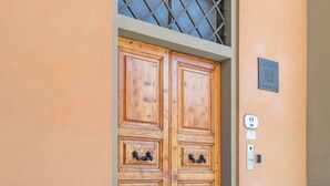 Una puerta doble de madera con una celosía metálica encima, ubicada en una pared color beige con una pequeña placa y un timbre.