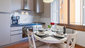 Una cocina moderna con armarios blancos, una estufa y una mesa de comedor preparada para cuatro, con platos, cubiertos y un florero con una flor roja.