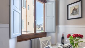 Un comedor con una mesa dispuesta para dos personas, una botella de vino y un jarrón con rosas rojas.