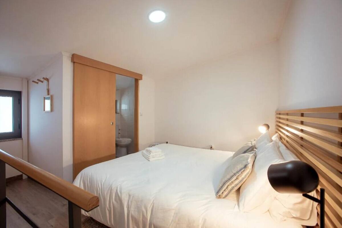 A bedroom with a bed, a wooden headboard, a nightstand, a mirror, and a door leading to a bathroom.