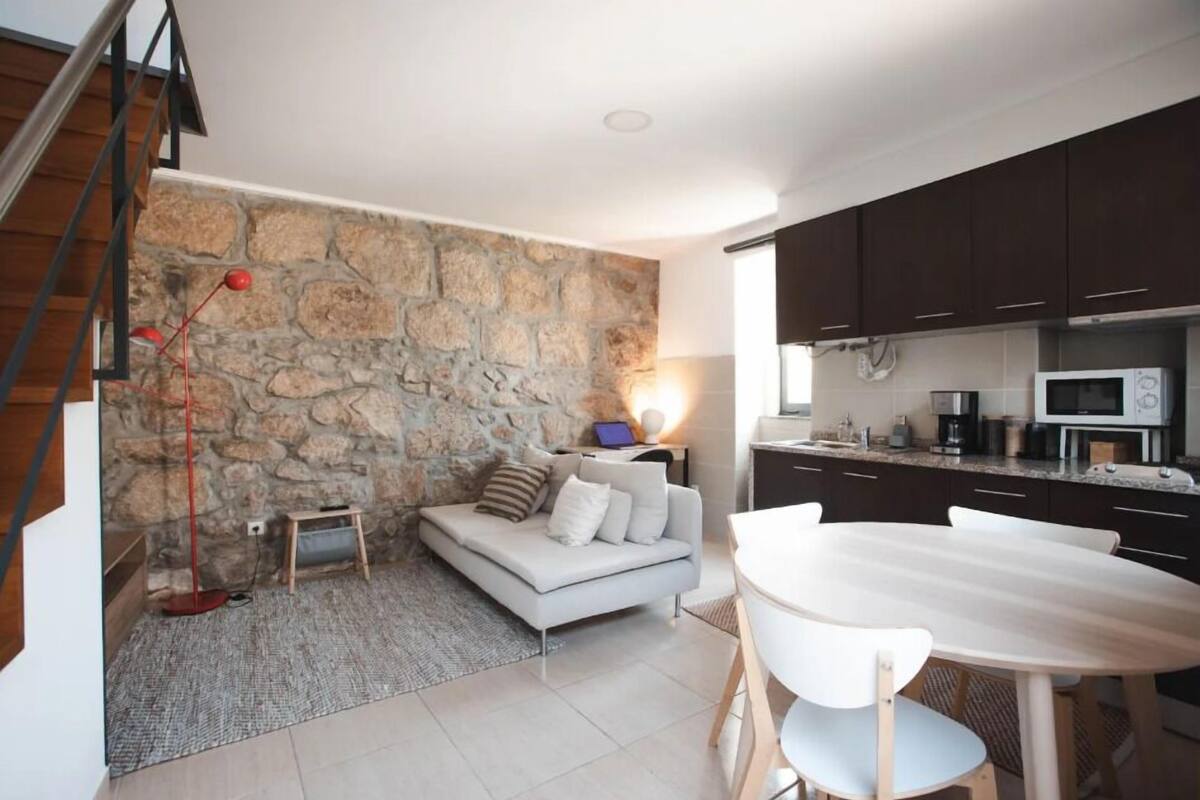 A modern kitchen with dark cabinets, a white countertop, and a microwave. There is a stone wall and a staircase leading to an upper level.