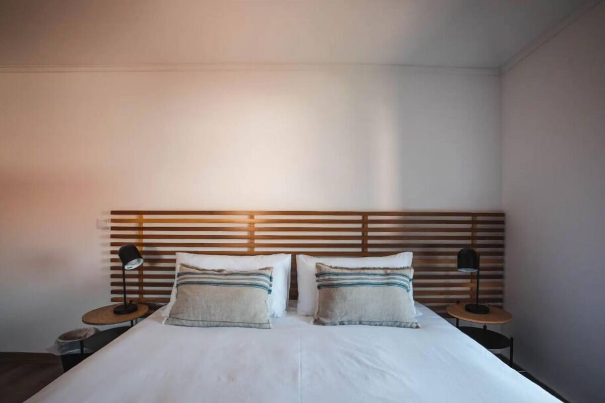 A neatly made bed with two pillows, a wooden slatted headboard, and two bedside tables with lamps.