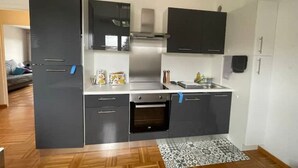 A compact kitchen with dark cabinets, a stainless steel range hood, a built-in oven, and a small countertop with a sink.