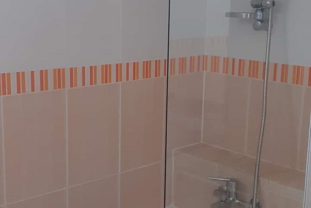 Un baño con cabina de ducha de vidrio, ducha de mano y suelo de baldosas.