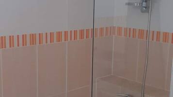 Un baño con cabina de ducha de vidrio, ducha de mano y suelo de baldosas.