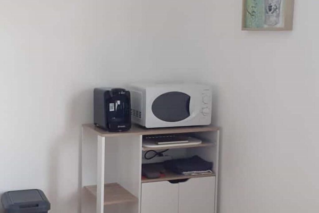 A small kitchenette with a microwave, coffee maker, and a shelf with various items.