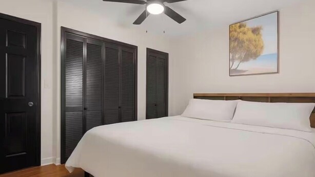 A bedroom with a bed, a ceiling fan, a door, and a framed picture on the wall.