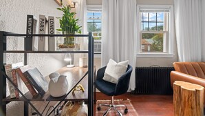 A modern living room with a bookshelf, a blue chair with a white cushion, a brown leather sofa, and a view of a house through a window.