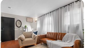 A living room with a beige armchair, a brown leather sofa, a wooden side table, and a white rug.