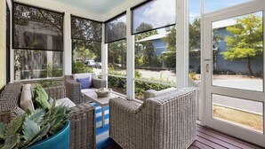 Une véranda meublée de mobilier en osier, dotée de grandes fenêtres et offrant une vue sur l’extérieur.