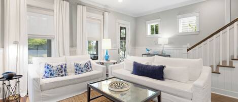 A living room with two white sofas, a glass coffee table, and a staircase.